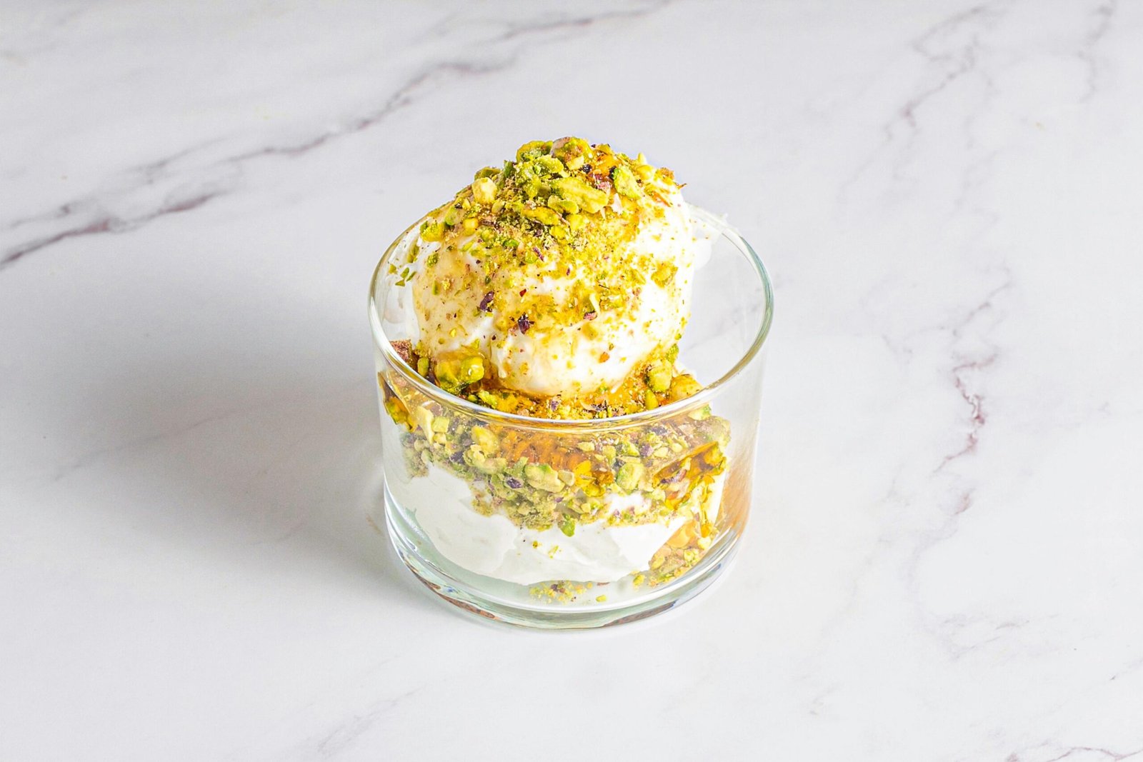 Postre libanés de yogur cremoso con miel y pistachos triturados, servido en vaso de cristal.
