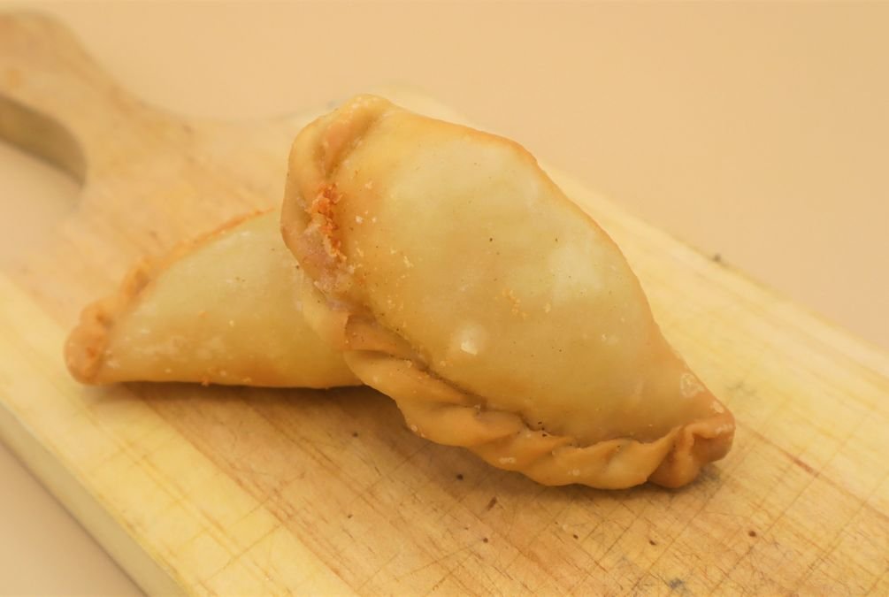 Empanadillas libanesas rellenas, doradas y crujientes, servidas sobre tabla de madera.